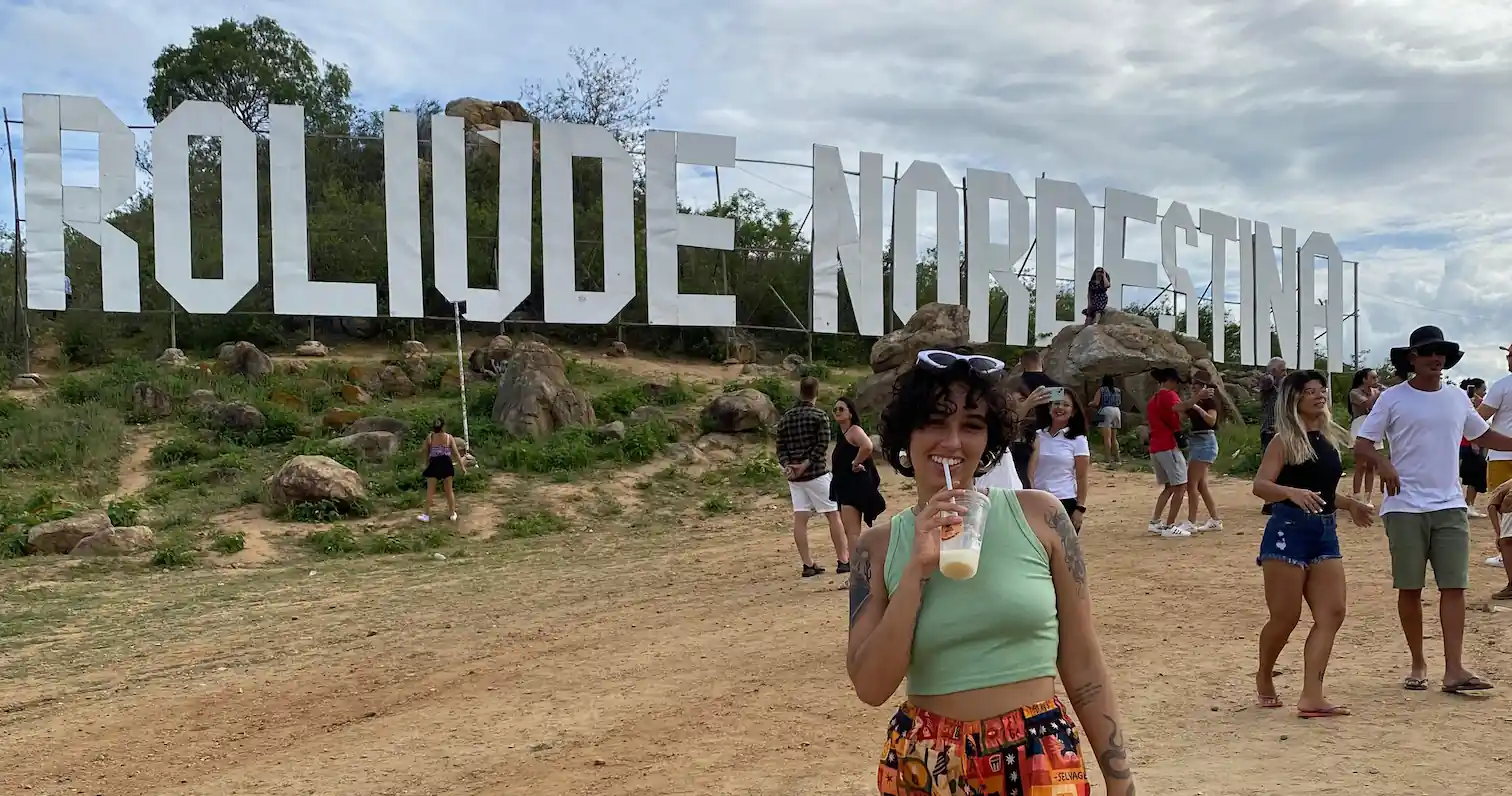garota morena de cabelos ondulados e curtos na frente da placa roliude nordestina em cabaceiras pb